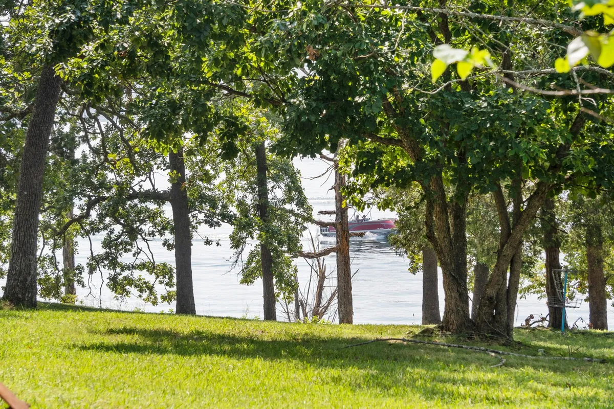 A serene view across glimmering water with lush green trees and a distant boat visible. The image exudes peace and relaxation, suggesting both active and leisurely lakeside experiences.