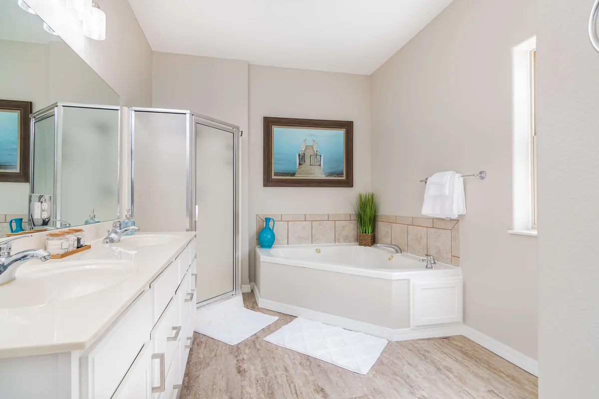 A bright and modern bathroom with a double vanity, large soaking tub, framed artwork, and a glass-enclosed shower. The space feels fresh and designed for relaxation.
