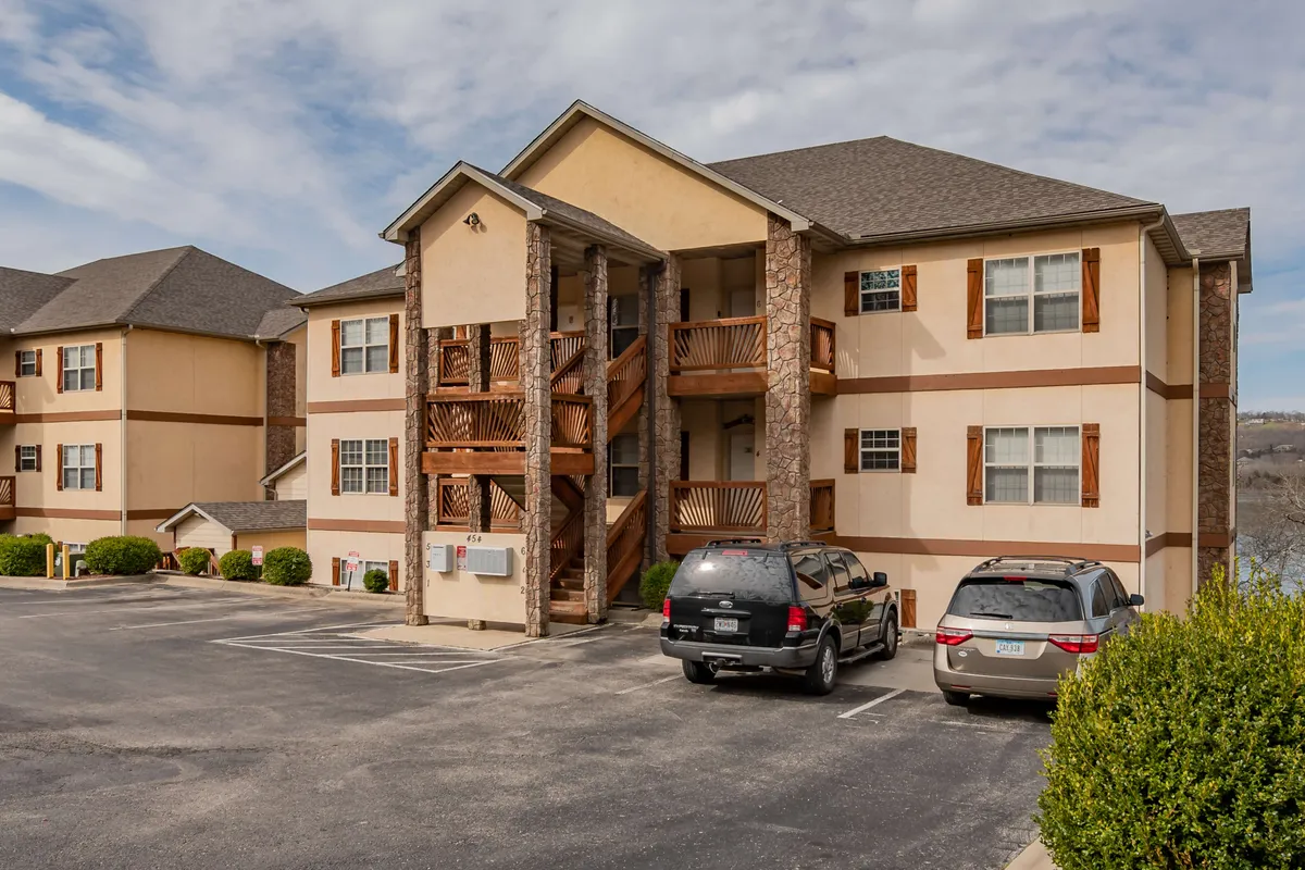 A view of balcony railings and stone pillars, with the surrounding landscaping and parking area visible. The scene is peaceful and inviting, suggesting a pet- and family-friendly environment for enjoying fresh air together.