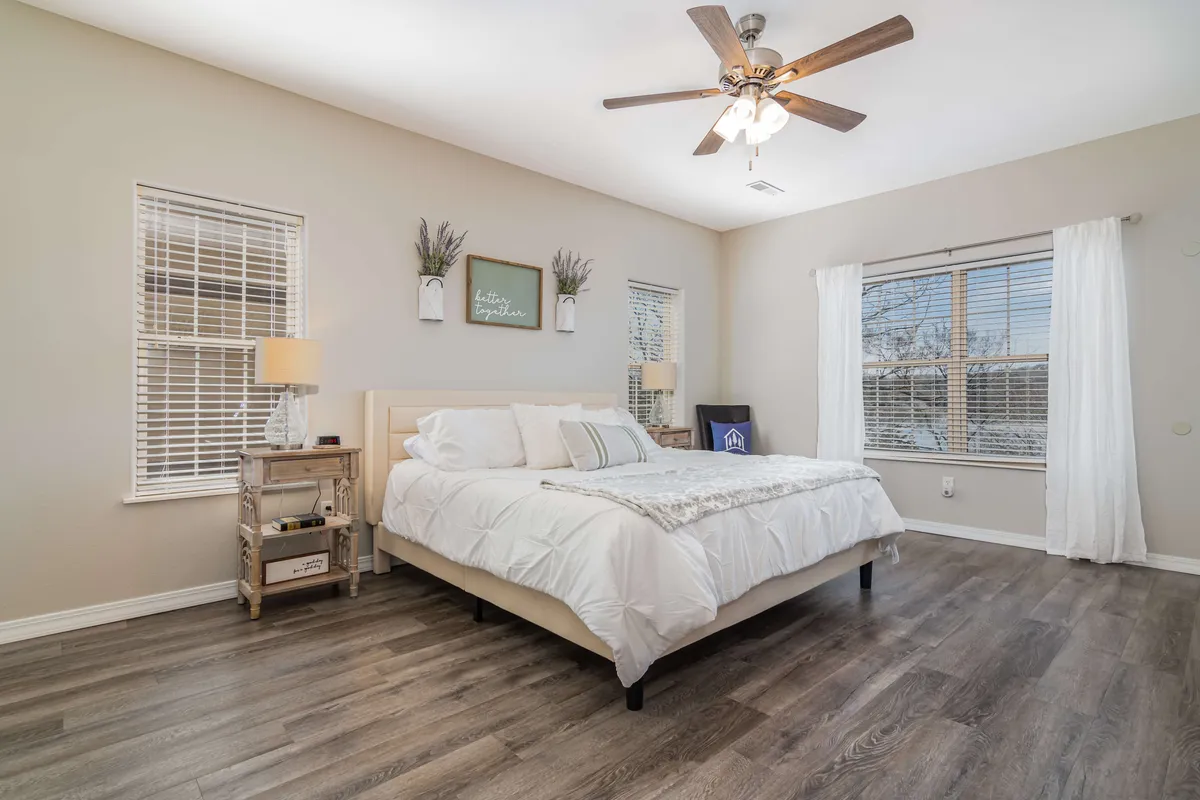 A serene bedroom featuring a neatly made king bed positioned between two nightstands, with windows letting in gentle natural light and decorative items providing a tranquil, inviting ambiance.