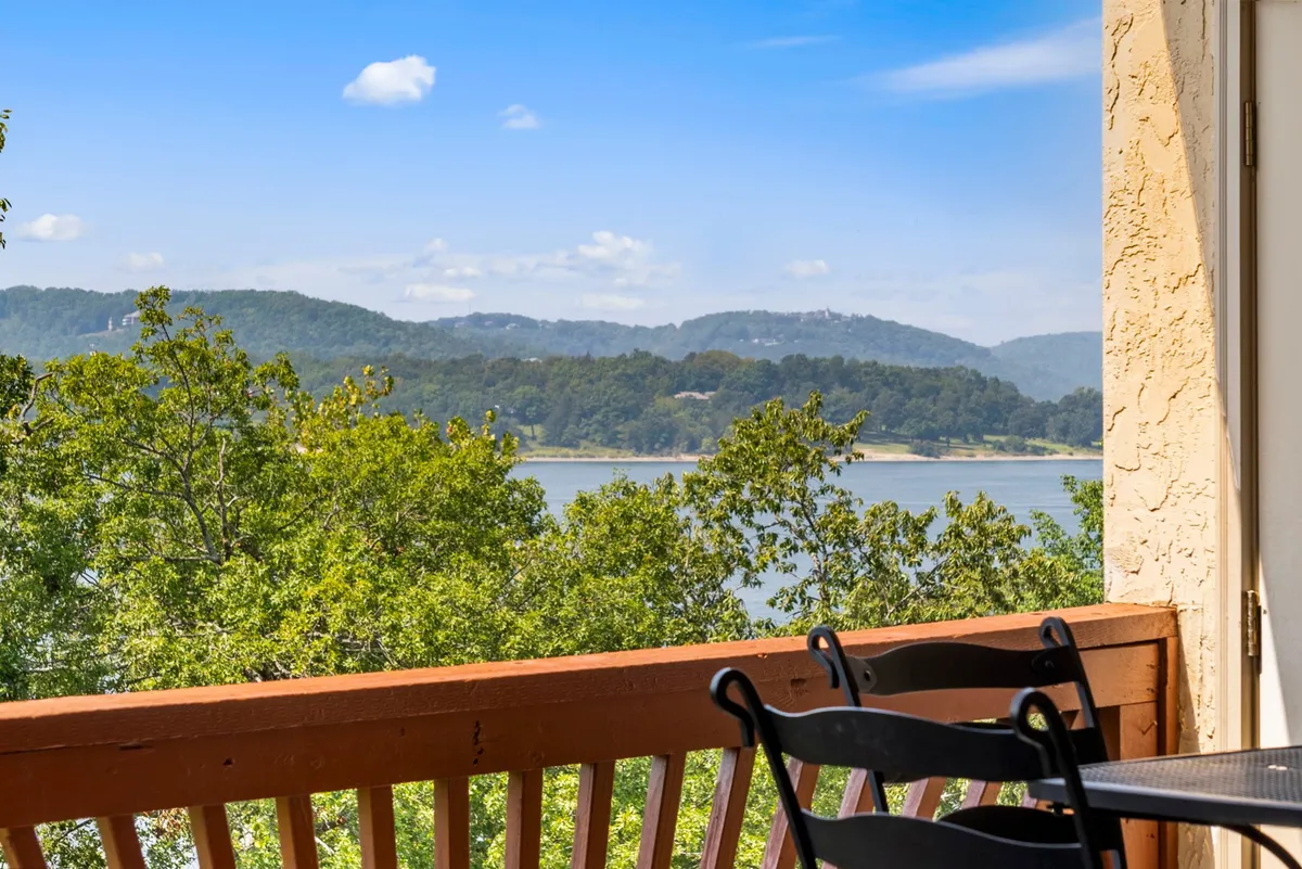 A stunning view from a balcony overlooking Table Rock Lake, framed by trees and gentle hills. The lake glistens under the sun, inviting guests to relax or set out for a day of aquatic adventures. The balcony railing subtly frames the scene, emphasizing the direct connection between the accommodation and the water.