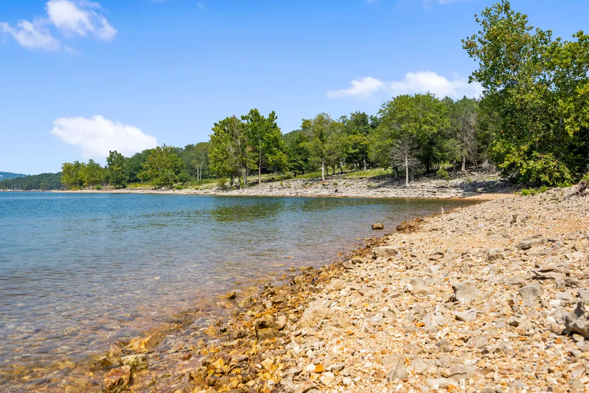 A tranquil scene of Table Rock Lake's rocky shoreline, bordered by lush greenery. The calm water invites activities like swimming, fishing, and sunbathing, while the natural surroundings evoke the peacefulness of lakeside living.