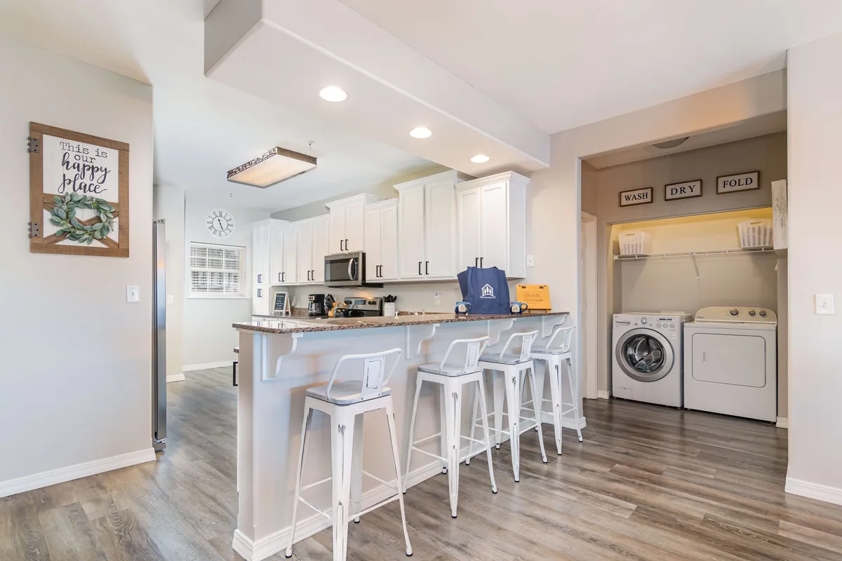 A cozy kitchen scene with a central island lined with bar stools, perfect for casual gatherings or meal prep with family and friends. The space is organized and inviting, with decorative wall art adding charm.