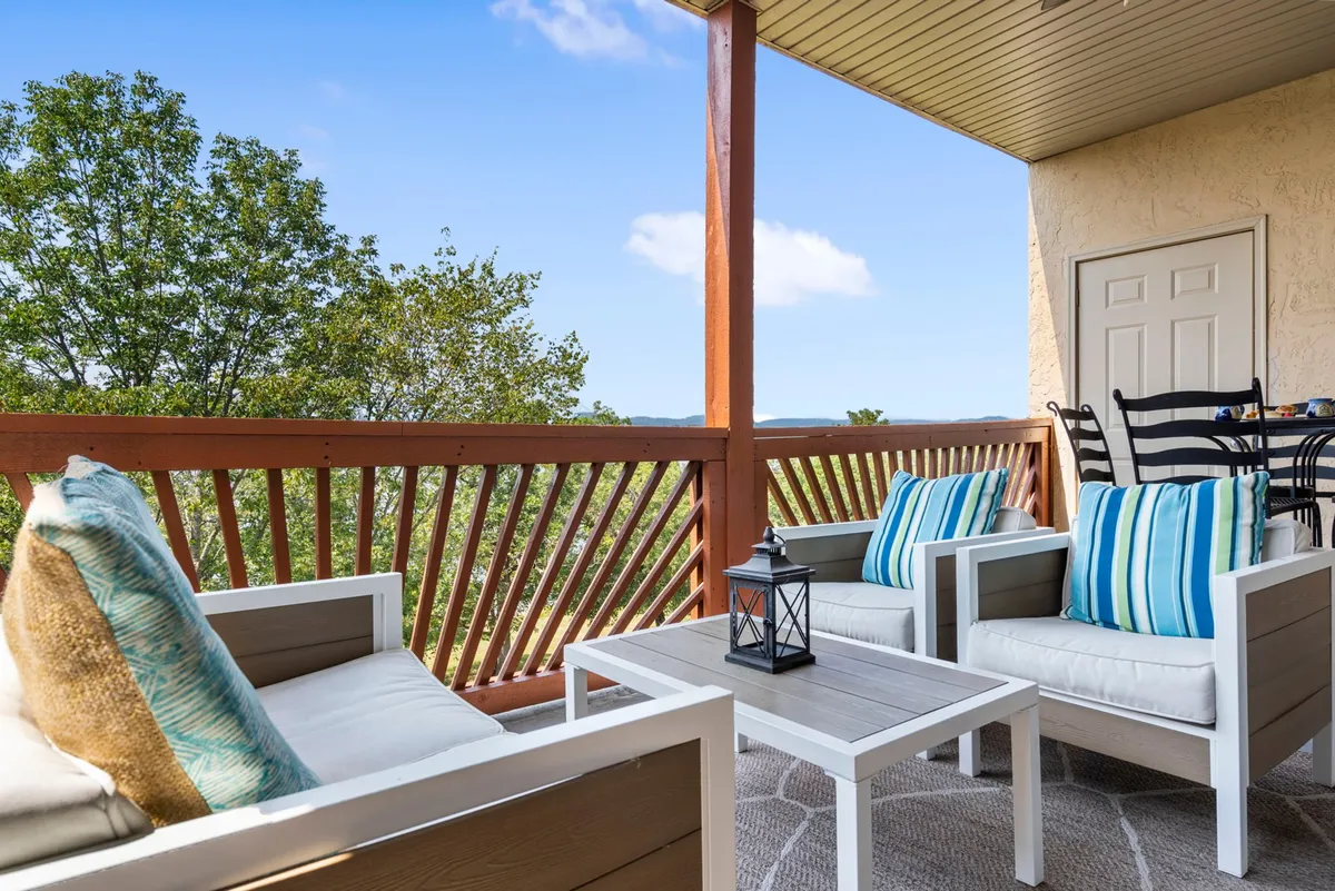 An outdoor seating area featuring striped cushions and a decorative lantern, set against a backdrop of trees and natural landscape. The space feels tranquil and inviting, ideal for relaxing with a pet after a lakeside walk.